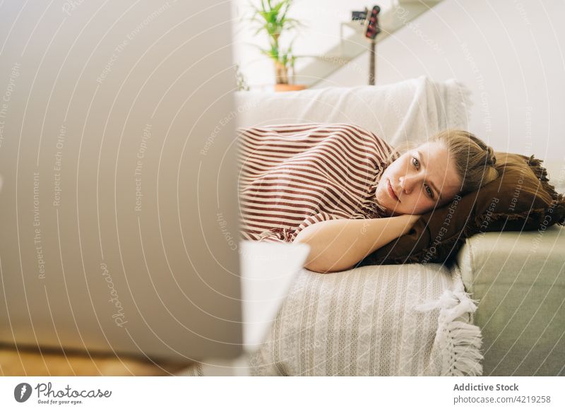 Tired woman watching film on laptop while resting on sofa movie weekend spare time tired using gadget device home plaid stripe ornament cushion soft lounge