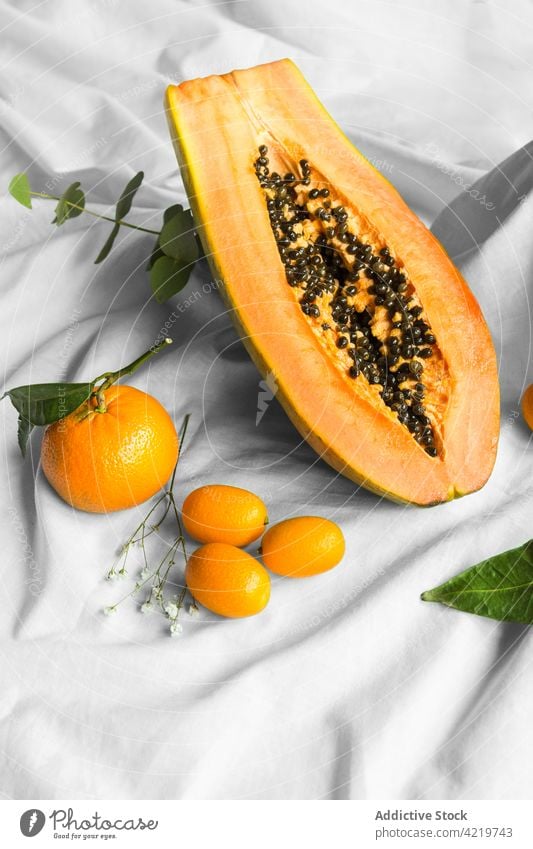 Cut papaya between mandarins and kumquats on creased fabric tangerine fruit tropical natural fresh vitamin leaf pawpaw cut half seed ripe juicy cumquat exotic