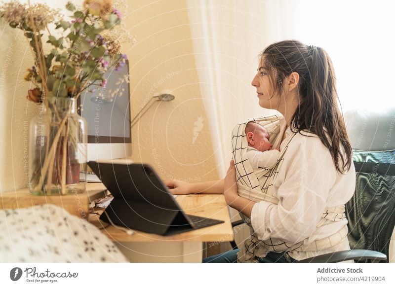 Mom holding baby and working on computer at home woman freelance newborn motherhood multitask desk notebook flower bonding write busy infant using study embrace