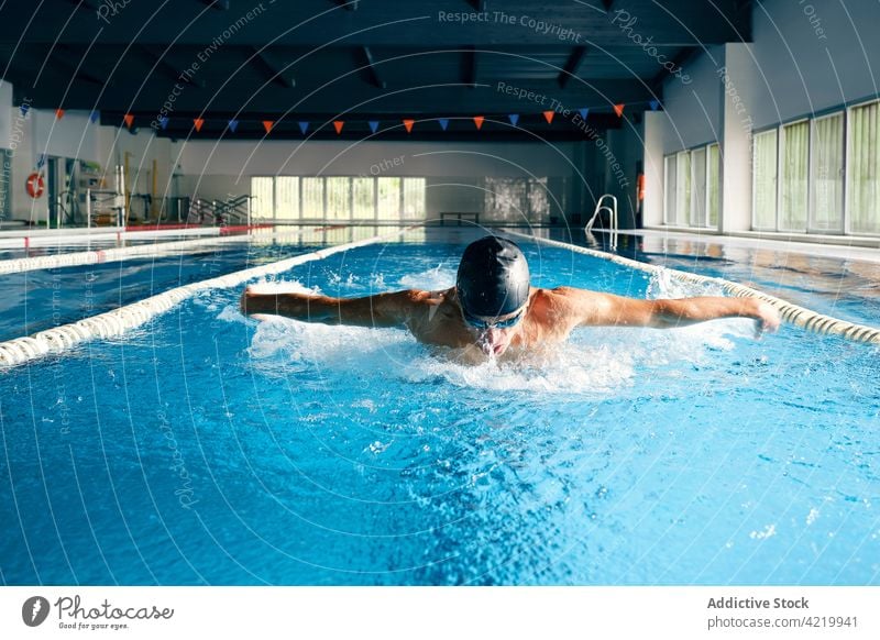 Sportsman in goggles swimming in pool during training swimmer butterfly stroke sport workout fast strong motion motivation power energy splash practice exercise