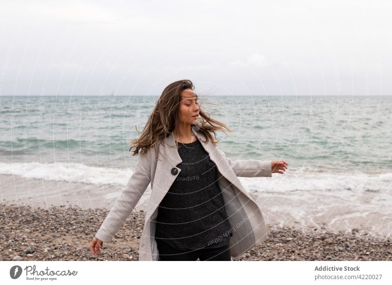 Carefree woman turning around at seaside carefree spin around dreamy autumn seashore tranquil enjoy female wind flying hair water calm harmony eyes closed