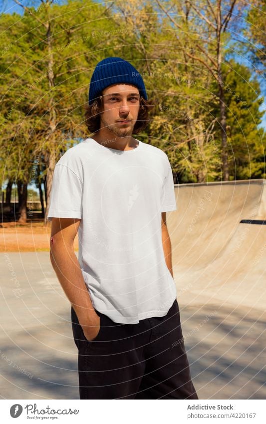 Portrait of a young man looking at camera Young skating skate blue portrait skateboard beanie hat pants fashion beard urban city t-shirt youth boy cool guy park