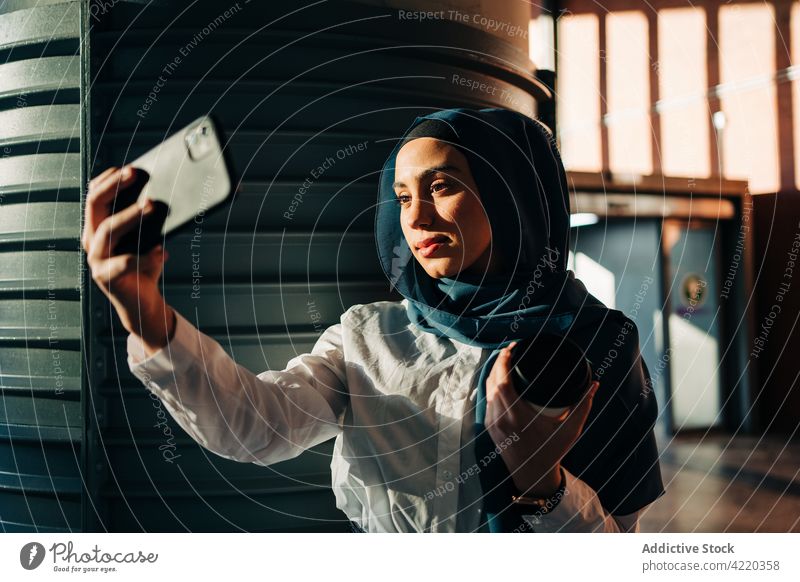 Muslim woman taking self shot on smartphone on train station selfie railway station hijab wait self portrait takeaway drink female ethnic muslim cellphone