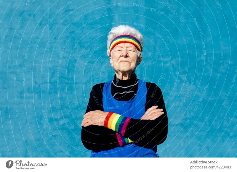 Senior woman in sportswear standing on blue background senior sportswoman colorful rainbow cool trendy elderly style female aged gray hair wristband headband