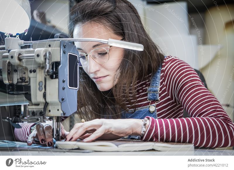 Seamstress sewing on sewing machine in workshop sewer woman upholstery cloth material workbench craftswoman female design professional occupation job busy