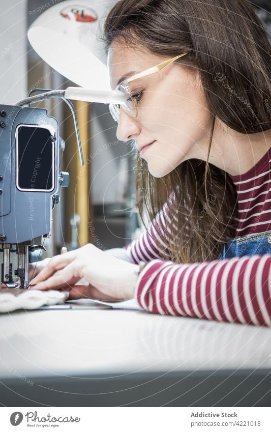 Seamstress sewing on sewing machine in workshop sewer woman upholstery cloth material workbench craftswoman female design professional occupation job busy