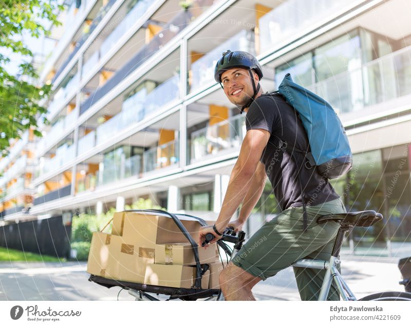 Bicycle messenger making a delivery on a cargo bike people young adult man male smiling happy blue collar Courier dispatch rider delivery man delivering package