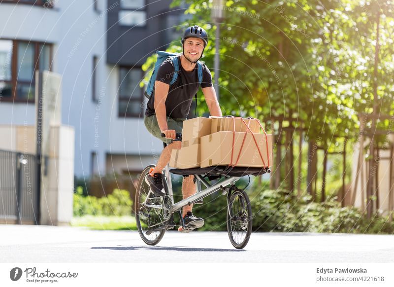 Bicycle messenger making a delivery on a cargo bike people young adult man male smiling happy blue collar Courier dispatch rider delivery man delivering package