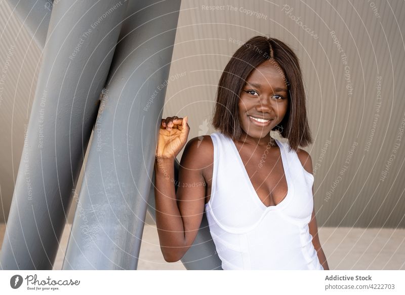 Smiling black woman standing near concrete poles style toothy smile trendy cool content appearance carefree charismatic outfit positive street happy sidewalk