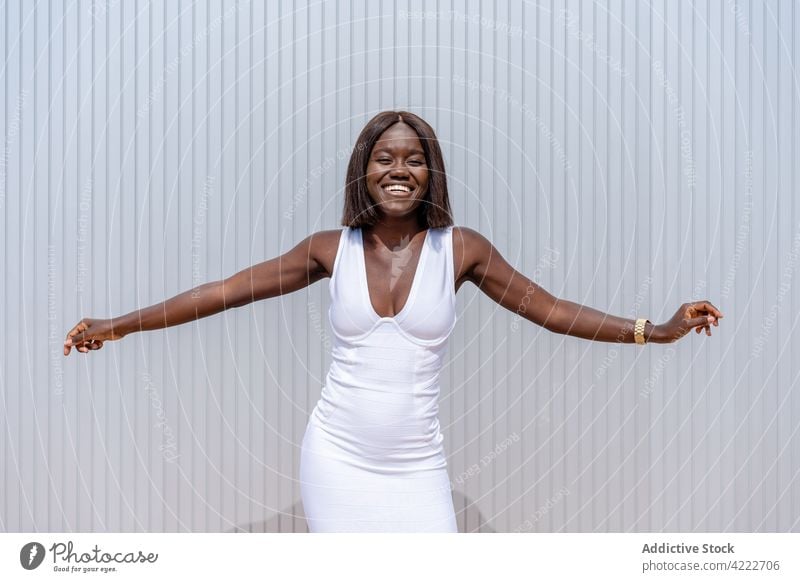 Joyful black woman outstretching arms on street sidewalk style joy trendy toothy smile expressive mood cool wall content appearance young outfit excited happy