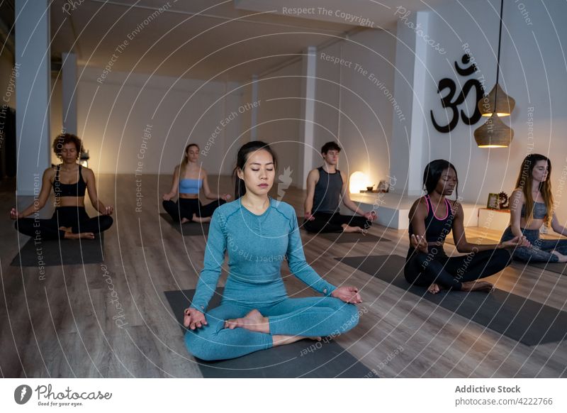 Peaceful multiethnic people meditating together during yoga lesson class meditate asian mindfulness zen lotus pose studio multiracial diverse eyes closed asana