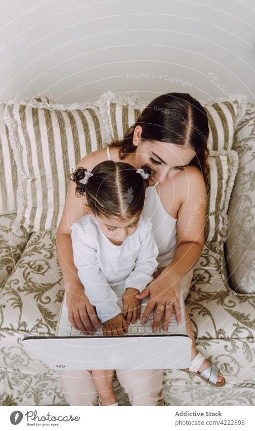 Mother and daughter watching movie on laptop mother child cartoon home little woman together ethnic sofa using girl kid gadget living room childhood internet