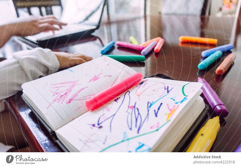 Crop mother and child at table with notebook and markers felt pen draw scatter messy drawing picture childcare kid sit together childhood little creative