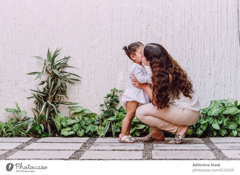 Mother kissing daughter in yard mother child little love tender motherhood gentle girl kid together childhood parent cute delicate plant green mom hug care