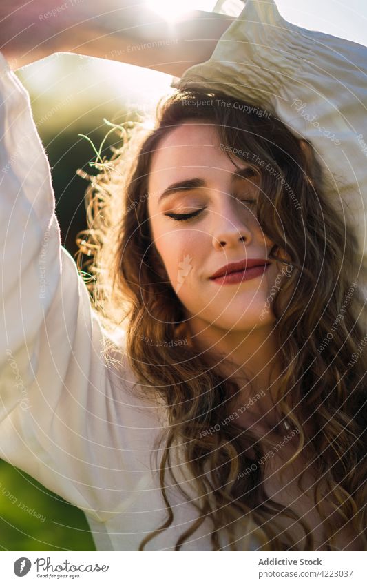 Smiling young woman in sunny nature cheerful gorgeous verdant grace arms raised content carefree happy optimist appearance positive delight curly hair park