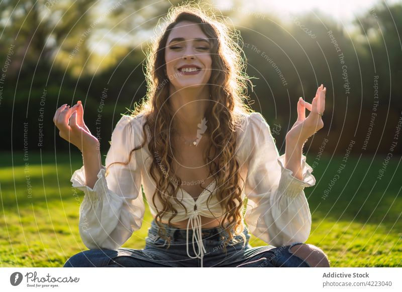 Smiling woman meditating in Lotus Pose in sunny park smile meditate lotus pose verdant yoga eyes closed mindfulness asana padmasana serene zen nature calm