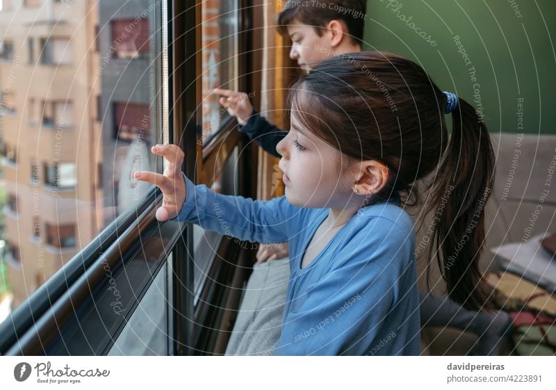 Two children in coronavirus lockdown drawing on the window girl writing with finger playing boring home quarantine apartment homewear writing glass kid