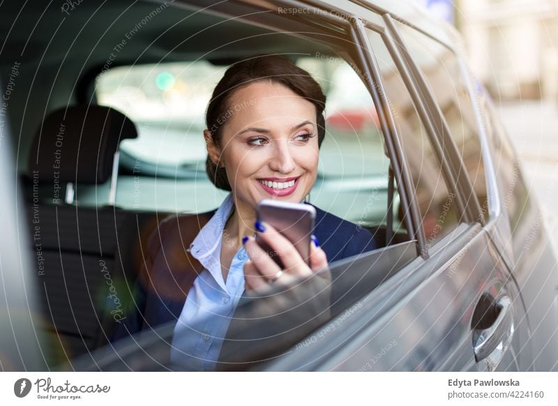 Young woman with smartphone on the back seat of a car carsharing confident smiling satisfaction female attractive beautiful young adult joy positive content