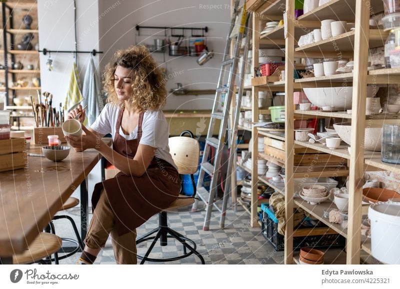 Craftswoman painting a bowl made of clay in art studio pottery artist ceramics work working people young adult casual attractive female happy Caucasian enjoying