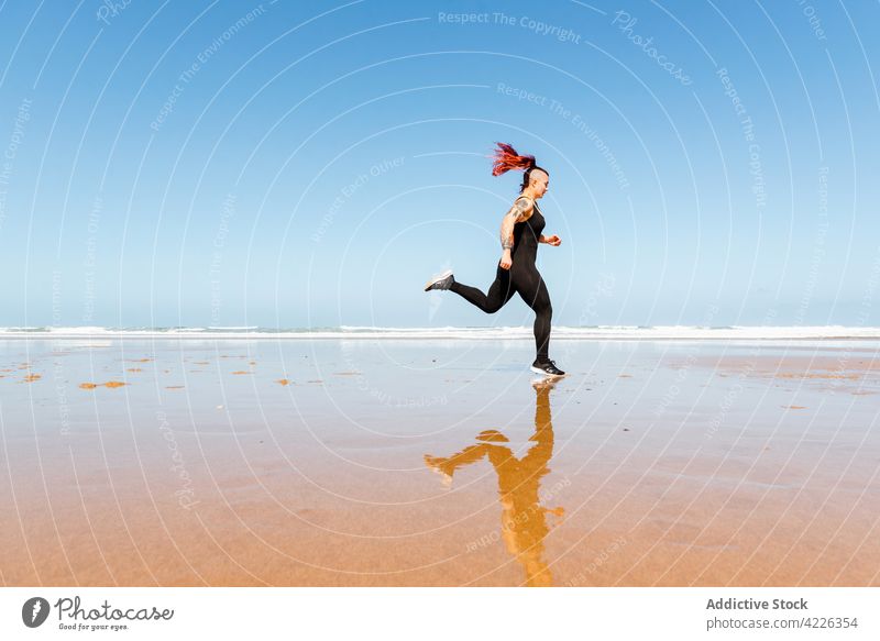 Fast runner jogging on sandy sea beach during workout jogger seashore sport training cardio activity tattoo woman reflection sportswoman exercise fast motion