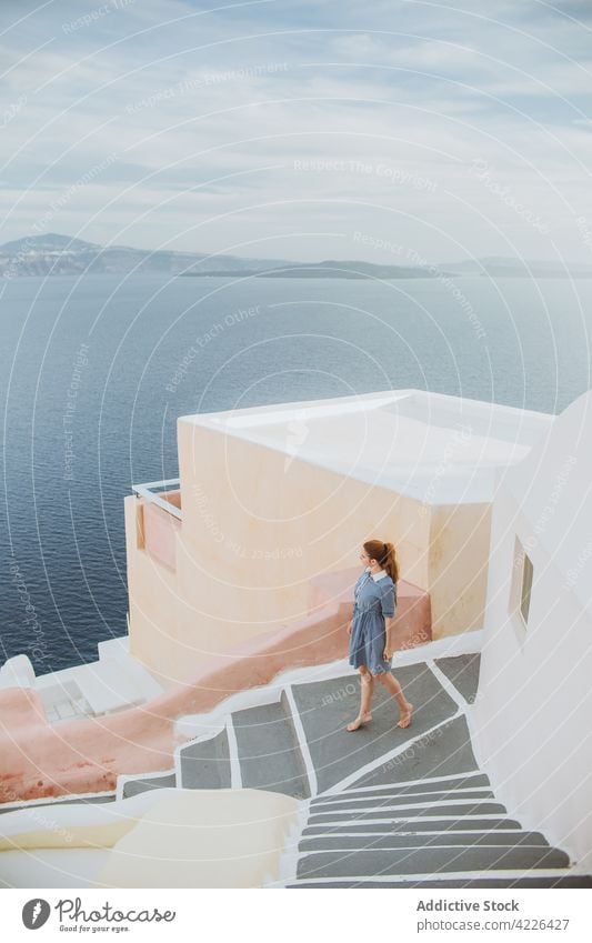 Unrecognizable woman standing on stone staircase in coastal village sea town oia village step architecture seacoast tourist weathered aged santorini greece