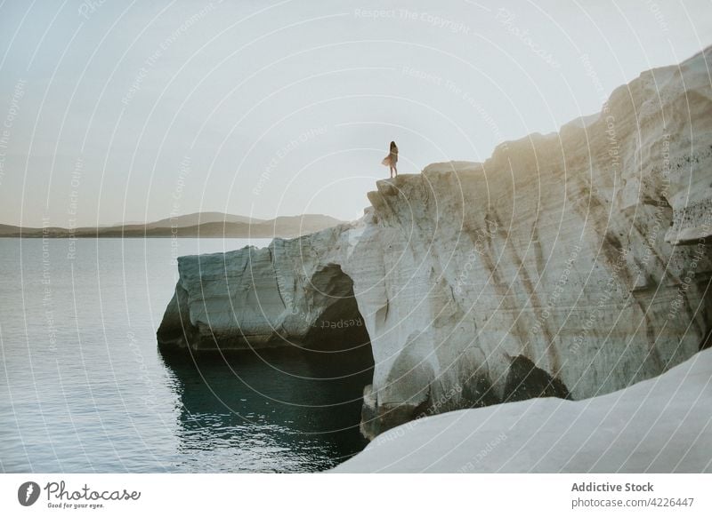 Faceless person standing on rocky cliff near rippling sea nature picturesque admire rough coast scenic stone tranquil idyllic ocean peaceful sarakiniko milos