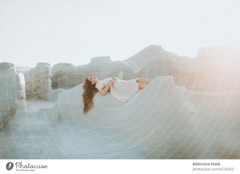 Serene woman lying on rocky stony formation in sunlight rough stone serene relax nature peaceful tender harmony geology young sundress sarakiniko milos greece