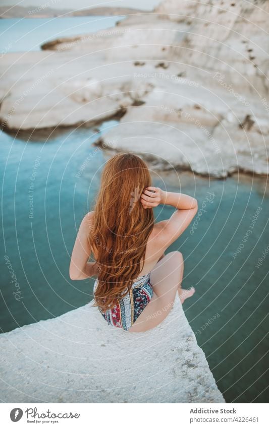 Anonymous woman in swimsuit resting on rocky cliff swimwear travel touch hair nature resort sunbath sea sarakiniko vacation suntan fit formation milos greece