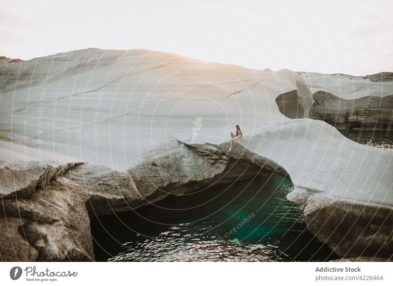 Distant woman in swimwear resting on picturesque uneven seacoast swimsuit seashore scenic sunny chill nature sunbath azure sarakiniko milos seaside paradise