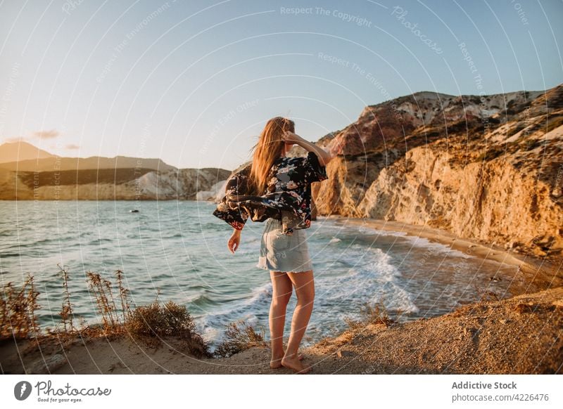 Unrecognizable woman standing on scenic rocky coast seashore nature touch hair resort coastline feminine picturesque cliff fyriplaka admire traveler style milos