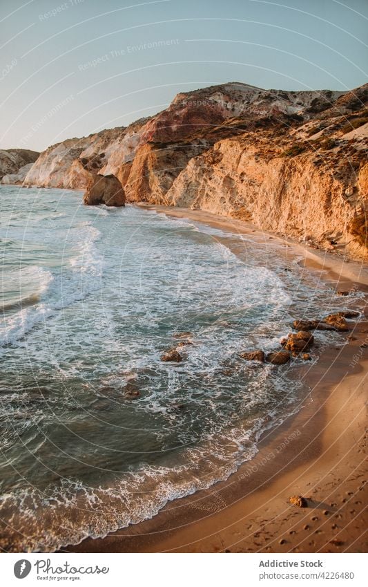 Scenic rocky seacoast near waving blue sea seashore nature uneven seafront picturesque scenic landscape bay fyriplaka milos blue sky rough wave ocean greece