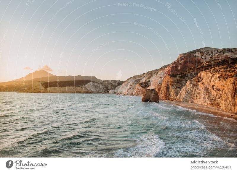 Scenic rocky seacoast near waving blue sea seashore nature uneven seafront picturesque scenic landscape bay fyriplaka milos blue sky rough wave ocean greece