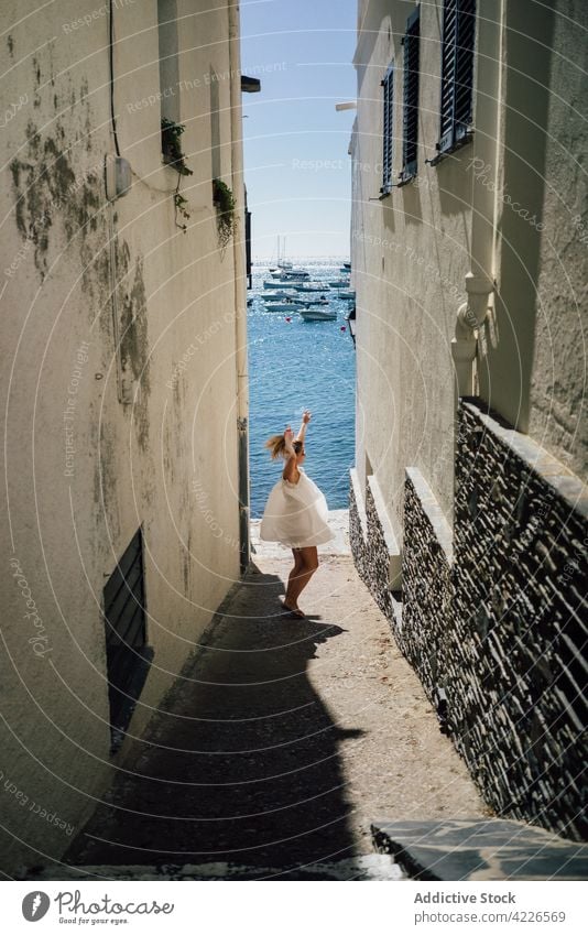 Unrecognizable excited traveler having fun against sea in town tourist dance arms raised vacation architecture building street woman freedom carefree house trip