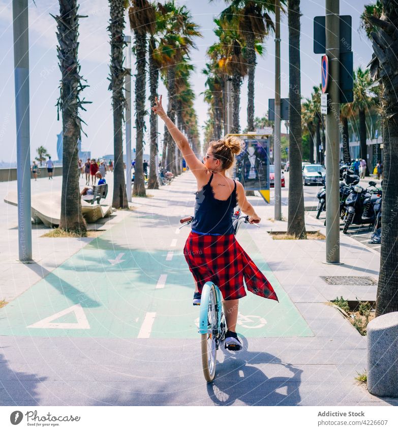 Biker riding bicycle and showing peace gesture on urban pavement biker ride two fingers route cool arm raised city woman direction victory checkered ornament