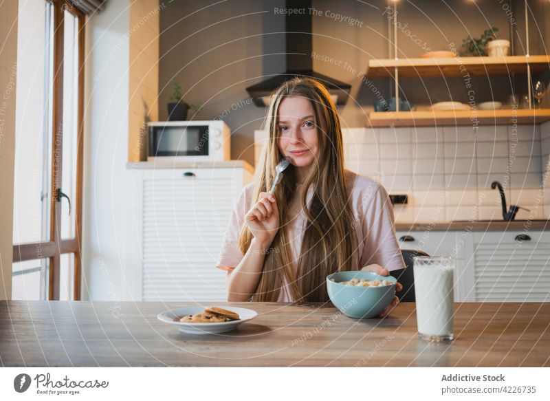 Woman eating delicious cereal for breakfast at home woman corn ring sweet nutrition mouth opened portrait kitchen portion table domestic spoon bowl enjoy