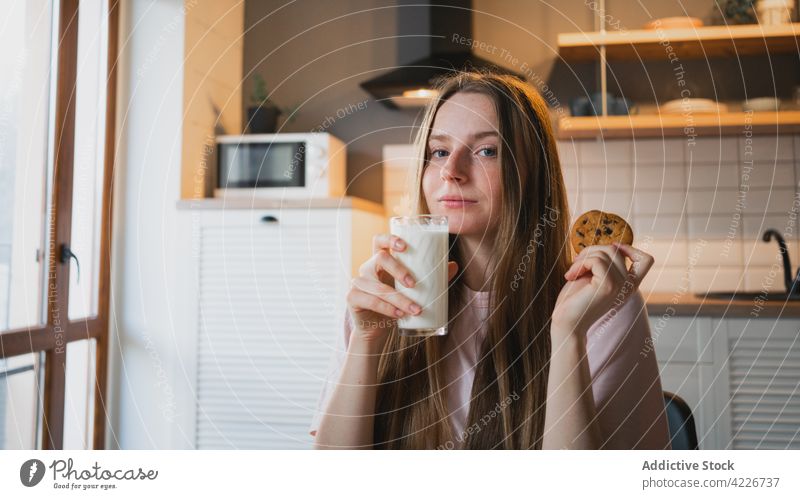 Smiling woman with delicious oat cookie at home treat chocolate chip sweet baked breakfast smile cheerful kitchen content glad scent beverage milk glass drink