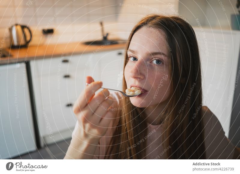 Woman eating delicious cereal for breakfast at home woman corn ring sweet nutrition mouth opened portrait kitchen portion table domestic spoon bowl enjoy