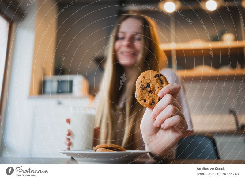 Smiling woman with delicious oat cookie at home treat chocolate chip sweet baked breakfast smile cheerful kitchen content glad scent beverage milk glass drink