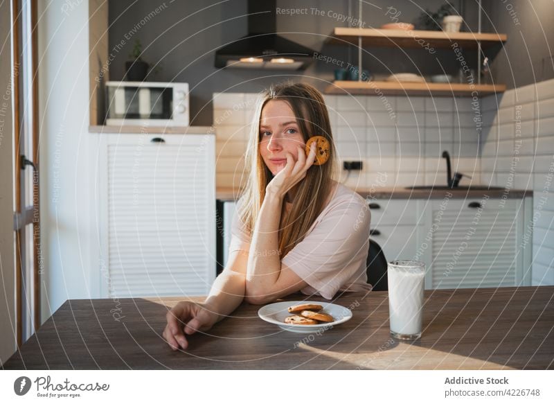 Smiling woman with delicious oat cookie at home treat chocolate chip sweet baked breakfast smile cheerful kitchen content glad scent beverage milk glass drink