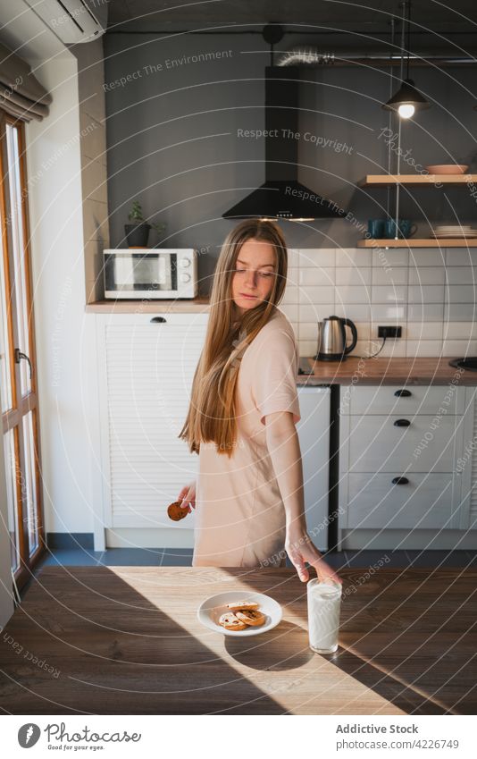 Woman with milk and oatmeal cookies for breakfast at home woman drink nutrient treat charming kitchen chocolate chip sweet baked contemplate wistful shadow