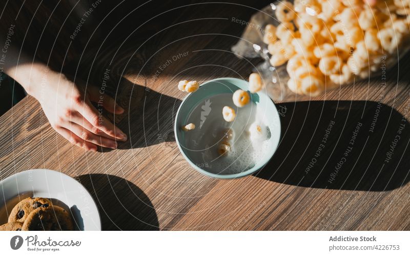 Crop person pouring milk into bowl with cereal breakfast corn delicious table flow dairy product crunchy tasty fresh morning nutrition yummy natural organic