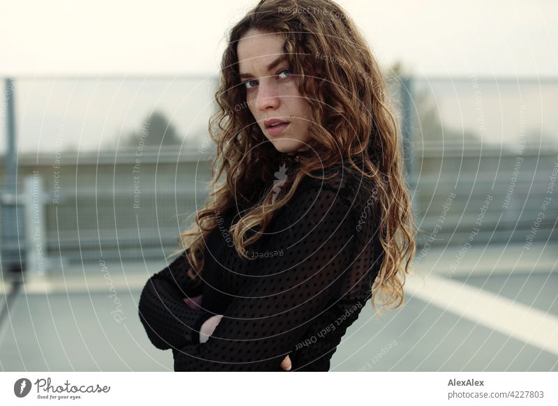 Portrait of a young woman with long, brunette, curly hair on the top parking deck of a parking garage Woman Young woman 18 - 30 years pretty Beauty & Beauty