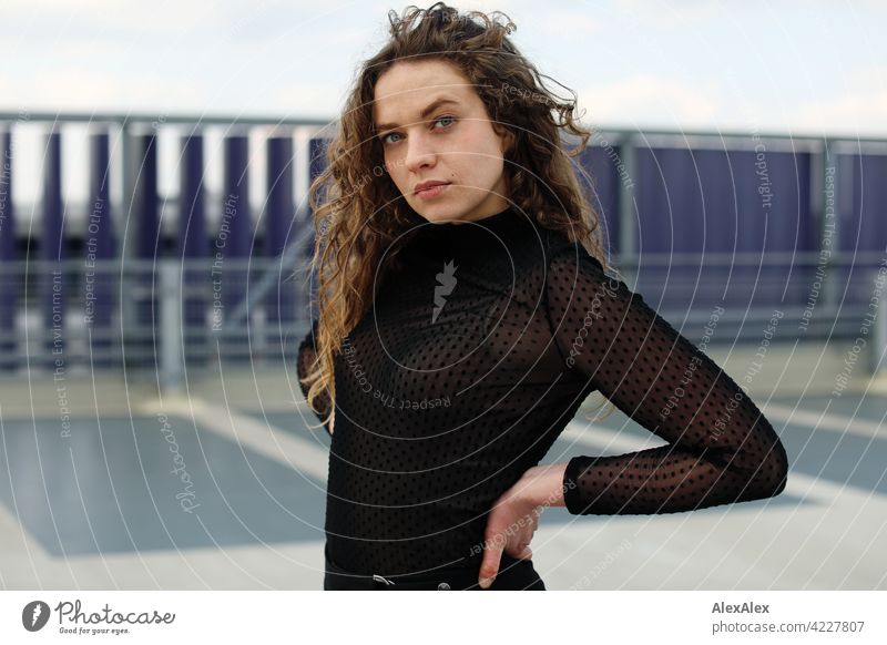 Portrait of a young woman with long, brunette, curly hair on the top parking deck of a parking garage Woman Young woman 18 - 30 years pretty Beauty & Beauty