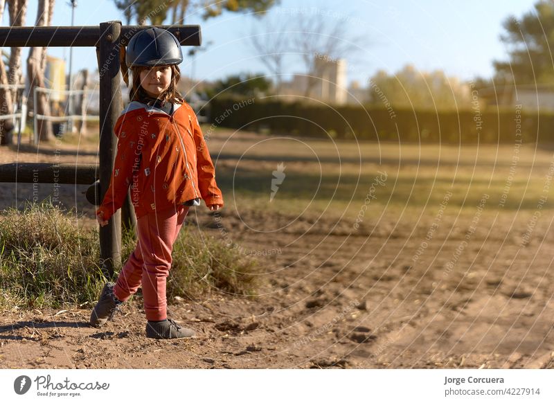 4 year old girl in horse riding dressed and ready to ride with nice posture and sunbeam. environment mixed between rural and urban animal beauty in nature cap