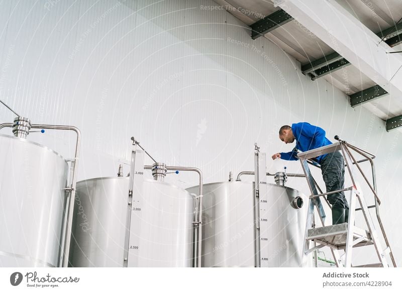 Brewer on ladder filling fermentation reservoir in beer factory brewer tank work industry man small business job liquid pour production professional