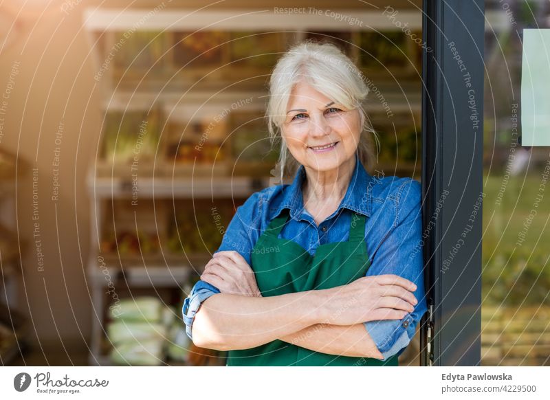 Senior woman working in small grocery store greengrocer groceries people senior mature adult casual attractive female smiling happy Caucasian toothy enjoying