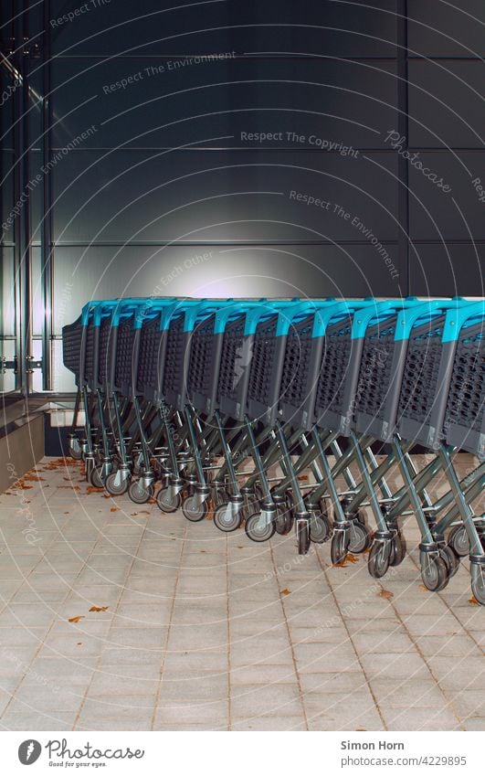 Row of shopping carts in front of grey wall. Shopping Trolley Supermarket Deposit everyday life shopping list Consumption Snake Parking lot on a daily basis