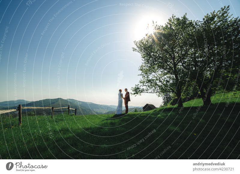 happy stylish bride and groom running and having fun in mountains on summer sunny day. gorgeous newlywed couple laughing, true feelings. emotional romantic moment.