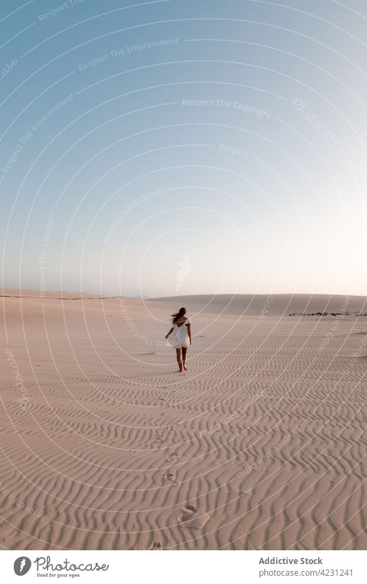 Unrecognizable traveler walking on sand in desert tourist trip vacation nature dune sky woman idyllic stroll summer tourism white dress feminine explore