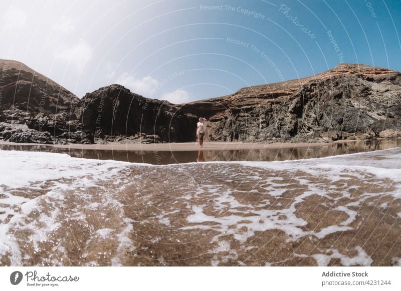 Unrecognizable traveler between rough mountain and foamy sea tourist nature highland landscape touch forehead woman blue sky cloudy ocean water transparent